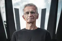 Portret starszego mężczyzny w okularach na tle nowoczesnej architektury.