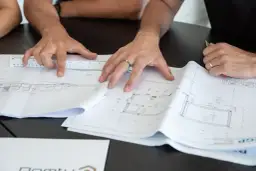 Des mains travaillent sur des plans d'architecte, une règle à la main. Comprendre ces détails est essentiel pour savoir pourquoi faire un devis précis.