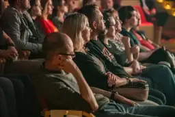 Widownia w teatrze siedząca w rzędach, skupiona na spektaklu.