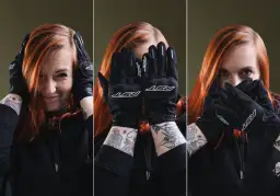Kobieta z rudymi włosami w czarnych rękawicach motocyklowych zakrywa twarz.