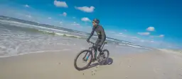 Rowerzysta przemierza piaszczyste plaże Słowińskiego Parku Narodowego. W tle błękitne niebo i fale Bałtyku.