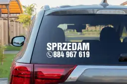 Nalepka na szybę samochodu z napisem "SPRZEDAM" i numerem telefonu.