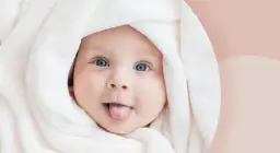 Urocze dziecko z niebieskimi oczami owinięte w biały kocyk, wystawiające język.