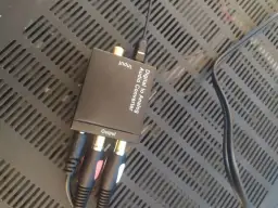 Konwerter cyfrowo-analogowy audio z podłączonymi kablami RCA i optycznym.