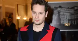 Krzysztof Zalewski, znany z charakterystycznego stylu, prezentuje się w stylowej marynarce. Jego wzrost jest imponujący, a spojrzenie przyciąga uwagę.