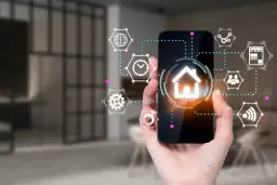 Dłoń trzyma smartfon z ikoną domu i otaczającymi go symbolami. To interfejs aplikacji spectrum smart, zarządzającej inteligentnym domem.