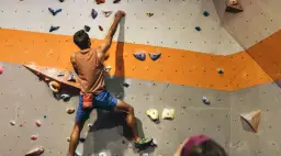 Mężczyzna wspina się po ścianie w hali do boulderingu. To świetny sposób na aktywność fizyczną i rozwijanie siły.