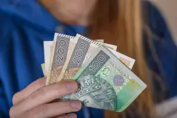 Dłoń trzyma polskie banknoty 100 i 200 zł. To symbol dodatku za wysługę lat w budżetówce.