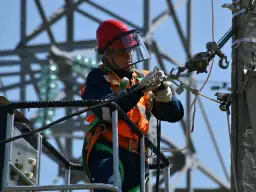 Elektryk w kasku i kamizelce odblaskowej pracuje na wysokości przy słupie energetycznym.