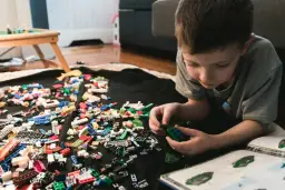 Chłopiec buduje z klocków LEGO, a obok leży instrukcja. Jak umyć klocki LEGO? Wystarczy je zebrać i umyć.