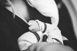 Dłoń noworodka chwyta ubranie mamy. Delikatne paluszki, które mogą wywołać **baby blues**, ale też ogromną miłość.