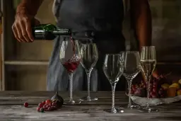 Skutki napowietrzania wina (dekantacja) widoczne podczas przelewania do karafki. Wino w kieliszku, obok winogrona i figi.