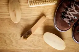 Cepillos y bota de piel de ante marrón sobre madera.