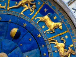 Złote figury Koziorożca i innych znaków zodiaku na niebieskiej tarczy zegara. 19 stycznia to czas Koziorożca.