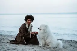 Kobieta z burzą włosów i biały pies na plaży. Idealne miejsce, gdzie nad morze z psem.