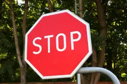 Ośmiokątny czerwony znak stop z białym napisem "STOP" na tle zielonych drzew.