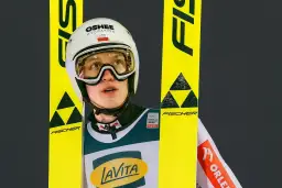Kacper Tomasiak wzrost – młody skoczek narciarski w kasku i goglach, otoczony żółtymi nartami Fischer.