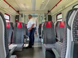 Wnętrze pociągu Polregio z siedzeniami i konduktorem. Zastanawiasz się, ile zarabia kierownik pociągu Polregio?