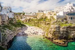 Malownicze klify i białe domy Polignano a Mare, z plażą pełną ludzi i turkusową wodą.