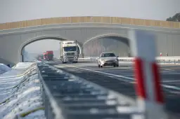 Autostrada A2 z mostem nad jezdnią, jadące samochody i ciężarówki w zimowej scenerii.