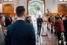 Panna młoda w welonie idzie do ołtarza z ojcem, wśród gości w kościele.