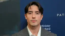 Dawid Kwiatkowski w szarym garniturze. Jego wzrost jest imponujący, a spojrzenie przyciąga uwagę.
