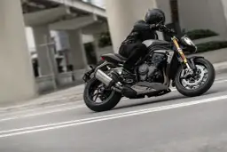 Motocyklista w kasku i skórzanej kurtce pochyla się na swoim motocyklu Triumph Speed Triple, pokonując zakręt na miejskiej drodze.