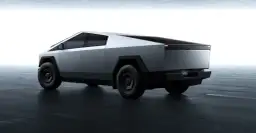 Futurystyczny Tesla Cybertruck w kolorze srebrnym, z ostrymi krawędziami i masywnymi kołami, prezentuje się na ciemnej, betonowej podłodze.