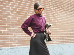 Mujer con gafas naranjas y blusa color burdeos, posando con un bolso de pelo.