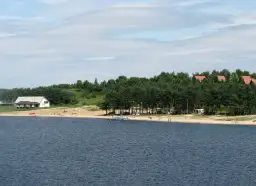 Słoneczny dzień nad zalewem Chańcza. Plaża z ludźmi, domki letniskowe i las.