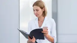 Koordynator medyczny w białej marynarce przegląda dokumenty i sprawdza telefon.