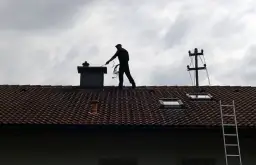 Kominiarz na dachu sprawdza komin. Zastanawiasz się, ile kosztuje przegląd kominiarski?