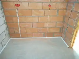 Przewody w posadzce bez peszla, przygotowane do dalszych prac instalacyjnych. Widoczne puszki instalacyjne w ścianie z cegły.