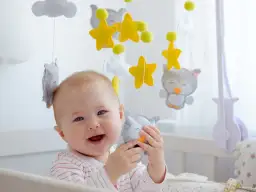 Uśmiechnięte dziecko bawi się wiszącymi zabawkami kontrastowymi od kiedy jest małe. Sowy i gwiazdki zachwycają malucha.