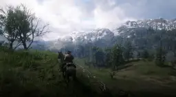 Jazda konno przez górzyste tereny w Red Dead Redemption 2 PC. Śnieżne szczyty gór i zielone lasy tworzą zapierający dech w piersiach krajobraz.