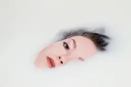 Rostro de mujer sumergido en leche, parte de un ritual de doble limpieza para una piel radiante.