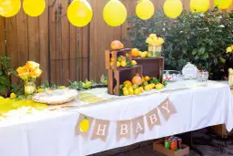 Udekorowany stół na baby shower z cytrynami, pomarańczami i żółtymi balonami.