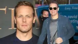 Sam Heughan, znany z roli w Outlander, w okularach przeciwsłonecznych i niebieskiej kurtce. W tle widać fragment logo i napis "covid testing".