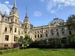 Imponujący pałac poznańskiego, z wieżyczkami i bogatymi zdobieniami, otoczony zielonym ogrodem z kwitnącymi krzewami róż.