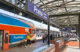 Pociąg z Gdańska do Pragi na dworcu głównym. Mężczyzna w żółtej kurtce z rowerem czeka na peronie.