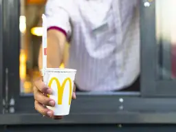 Ręka podaje kubek z McDonald's. Zastanawiasz się, ile kalorii ma cola zero z McDonald's? Ten napój ma zero kalorii.