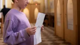 Młoda osoba w fioletowej bluzie trzyma kartkę, przygotowując się do spowiedzi świętej w kościele.