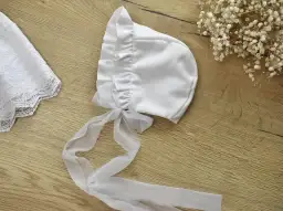 Elegancka, biała bonetka do chrztu z tiulową kokardką i koronkowym wykończeniem.