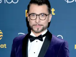 Kacper Kuszewski w fioletowym aksamitnym smokingu z czarną muszką. Wygląda elegancko, jakby wybierał się na galę, gdzie może spotkać swoją żonę.