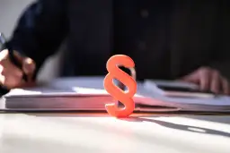 Czerwony znak paragrafu na biurku, symbolizuje prawo i sprawiedliwość. Obok stos dokumentów, gdzie prawnik przygotowuje nagrodę jubileuszową.