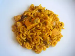 Fideuà de pollo con fideos rizados y trozos de pollo en salsa dorada, servida en plato blanco.