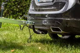 Montaż haka holowniczego w czarnym Volvo. Przyczepa gotowa do drogi, zielona trawa i krzewy w tle.