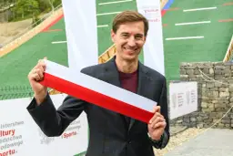 Uśmiechnięty mężczyzna trzyma biało-czerwoną wstęgę. Czy to symbol otwarcia obiektu, który ma ile lat stoch?
