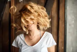Uśmiechnięta dziewczyna z burzą włosów w odcieniu maślany blond, które wirują wokół jej twarzy.