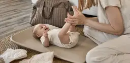 Uśmiechnięte dziecko na przewijaku, który znajduje się na wygodnej wysokości. Obok torba i pieluszki.